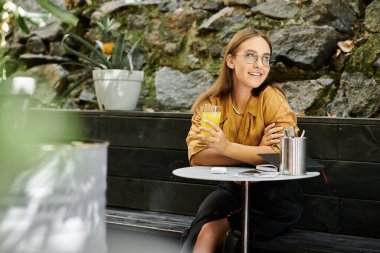Büyüleyici bir kafe ortamında, genç bir kadın ferahlatıcı bir içki yudumluyor, protez bacağını gösterirken neşe ve güven saçıyor..
