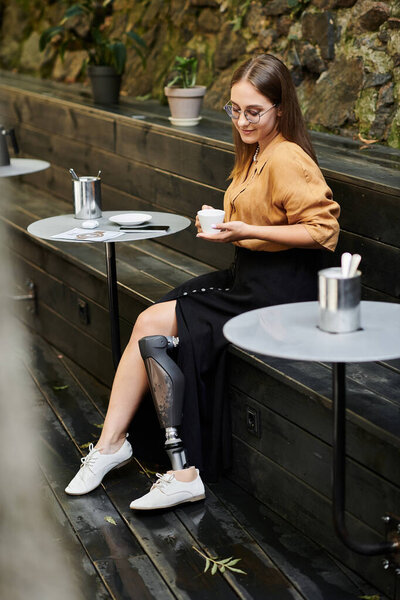 В уютном кафе молодая женщина с протезной ногой с любовью пьет кофе, разделяя момент радости и стойкости..