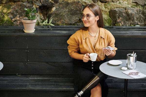 Уверенная в себе молодая женщина сидит в уютном кафе, потягивая кофе и обнимая свою повседневную рутину протезной ногой.