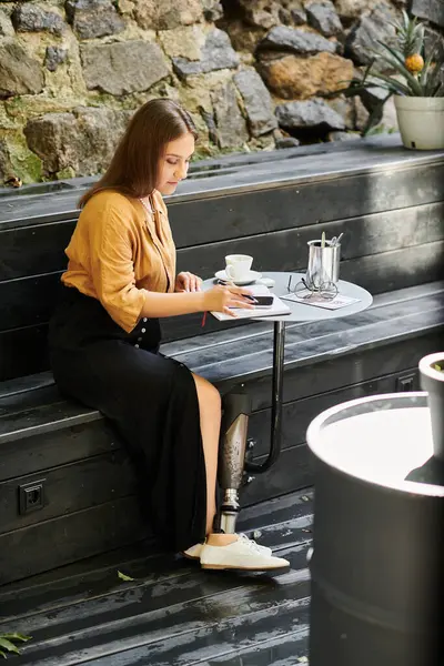 stock image A young woman comfortably sits in a cafe, sipping coffee while engaging with her smartphone, radiating positivity.