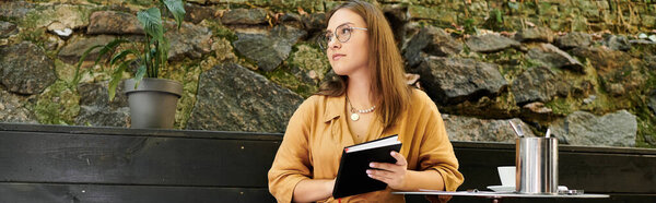 Молодая женщина удобно сидит в кафе, погруженная в свой блокнот, наслаждаясь атмосферой.