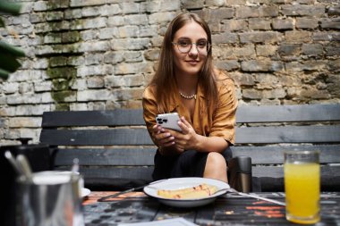 In a charming cafe, a young woman with an artificial limb savors her time, enjoying a meal and staying connected on her smartphone. clipart