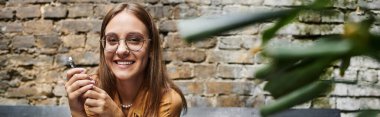 In a cozy cafe, a young woman smiles while holding smartphone clipart