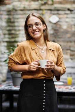 A young woman smiles warmly while sipping coffee at a bustling cafe, enjoying her day. clipart