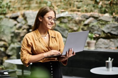 A young woman engages in her daily routine, delightfully focused on her laptop in a vibrant cafe. clipart