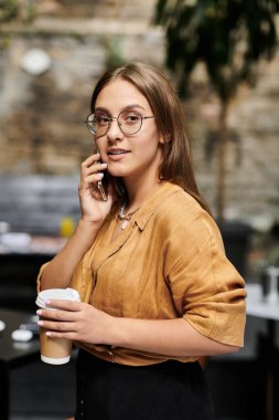 Telefonla konuşan genç bir kadın, hayat dolu bir kafe atmosferini kucaklıyor..