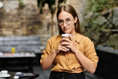Bir kafe ortamında, genç bir kadın elinde kahve fincanı tutarak günün tadını çıkarırken kendine güveni yayar..