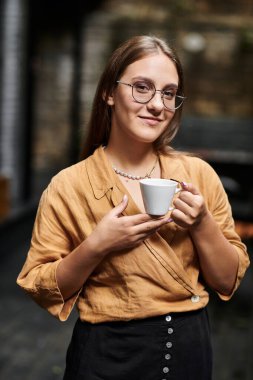 Sıcak bir kafe ortamında, genç bir kadın bir fincan kahve tutuyor, günlük hayatı kucaklıyor..
