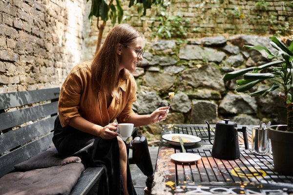 Молодая женщина удобно сидит в кафе, наслаждаясь кофе и закуской, демонстрируя свой яркий образ жизни с искусственной конечностью..