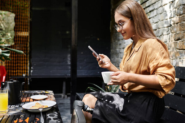 В оживленном кафе молодая женщина с искусственной конечностью потягивает кофе и прокручивает свой телефон, обнимая повседневные моменты.