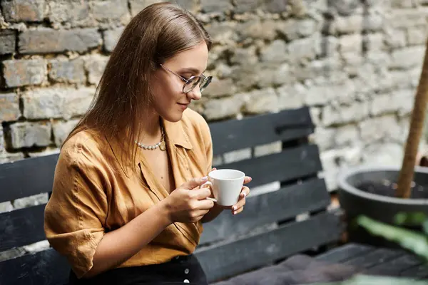 stock image A young woman sits comfortably in a caf, sipping coffee while showing her artificial limb with a calm demeanor.