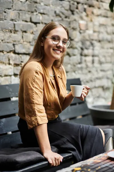 stock image A young woman with an artificial limb sits comfortably in a cafe, savoring her coffee while smiling warmly at the camera.