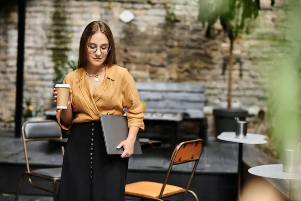 stock image In a cozy cafe, a young woman confidently balances her drink and laptop, showcasing her vibrant daily life.