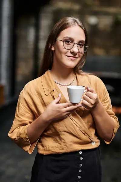 stock image In a warm cafe setting, a young woman holds a cup of coffee, embracing daily life.