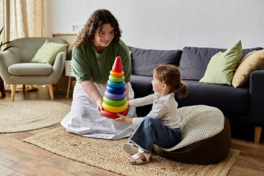 A mother and daughter share laughter while stacking colorful rings on a cozy afternoon. clipart