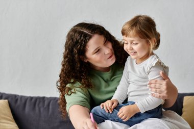 A loving mother engages with her daughter, sharing smiles and creativity in a cozy living space. clipart