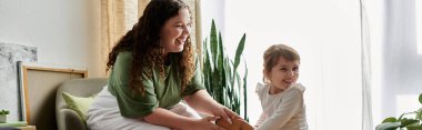 A beautiful plus size woman and her daughter share laughter and joy while playing together indoors. clipart