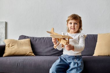 Little cute girl playing with her toy plane at home. clipart