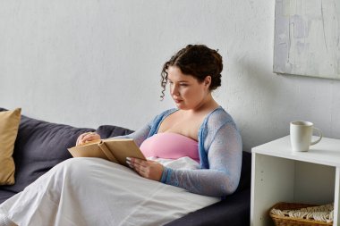 Evinde, elinde kitap tutan rahat ev kıyafetleri içinde güzel bir genç kadın..