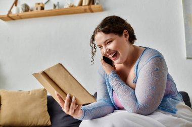 Ev kıyafetleri içinde neşeli genç bir kadın. Ellerinde kitap tutuyor, evinde..