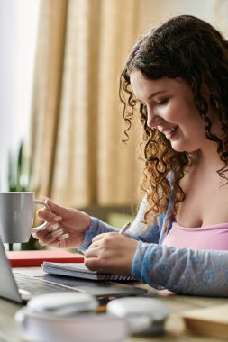 Cheerful plus size woman with curly hair in cozy attire working at home. clipart