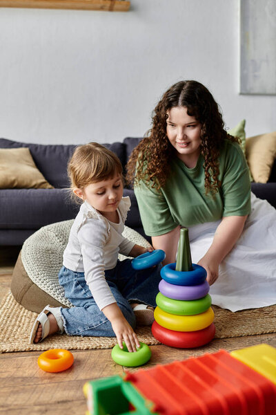 Играющий момент разворачивается, когда мать и дочь наслаждаются складыванием разноцветных колец вместе.