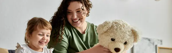 stock image A lively moment of a plus size mother and her daughter enjoying playtime together with a teddy bear.