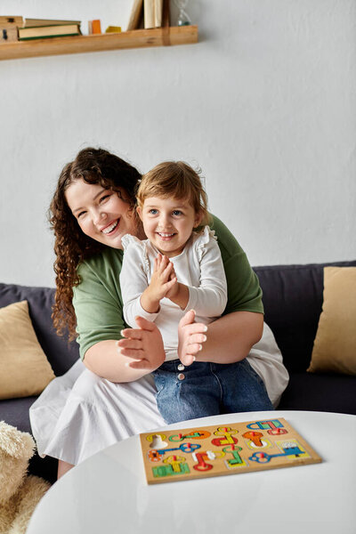 A mother and daughter share laughter while playing with a colorful puzzle on the table.
