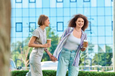 İki neşeli arkadaş dışarıda birlikte yürürken gülüşür ve sohbet ederler..