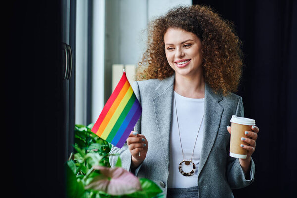 A coworker holds a rainbow flag with a smile and coffee, embracing inclusion and diversity.