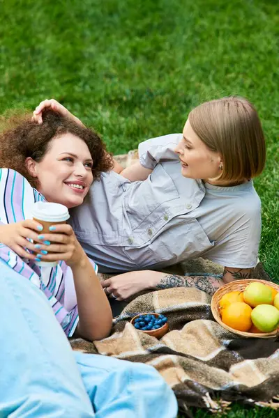 stock image Two young women share laughter and stories while enjoying snacks on a sunny day outdoors.