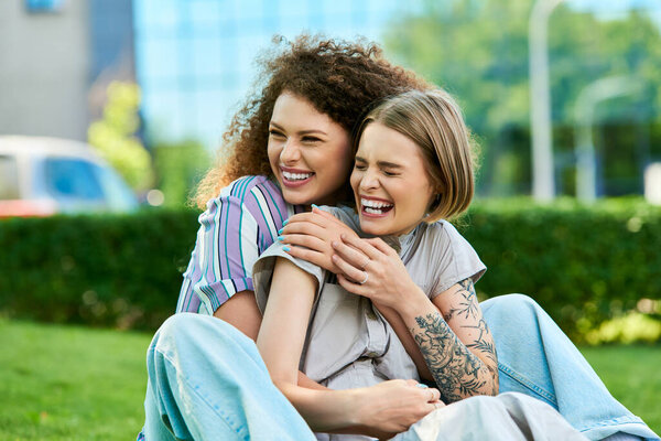 Enjoying a playful moment, two friends embrace each other while laughing in a green park.