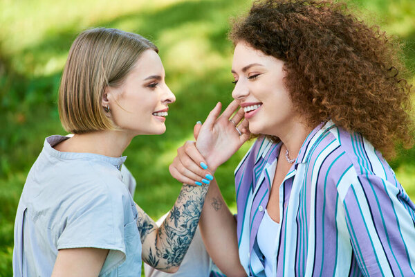 Two young women share a joyful moment, laughing and connecting in a vibrant green park.