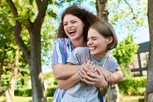 Two young women share joyful moments and laughter while embracing in a lush green park.