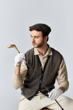 Klasik golf kıyafeti giymiş şık bir adam, golf sopasına zarafet ve özgüvenle hayran kalır..