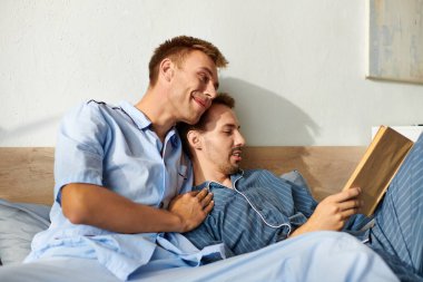 Pijamalı iki adam, sıcaklık ve şefkat ile çevrili bir kitaba dalmış, yumuşak bir sabahı paylaşıyorlar..