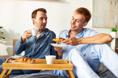 Neşeli bir eşcinsel çift pijamalarıyla kahvaltıyı sever, birbirlerine eşlik ederler ve lezzetli ikramların tadını çıkarırlar..