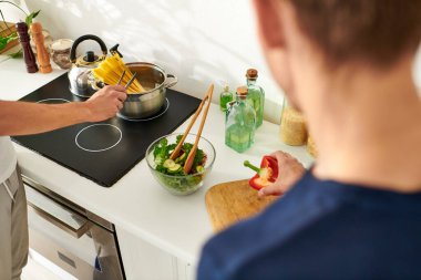 A loving couple collaborates in a contemporary kitchen, chopping vegetables and creating a vibrant salad. clipart