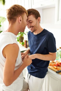 A loving gay couple interacts warmly as they chop fresh vegetables together in a stylish kitchen. clipart