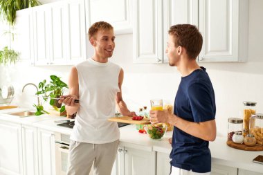 Neşeli çift, renkli bir salata için sebze keserken yemek pişirir, kahkahalarını paylaşır..