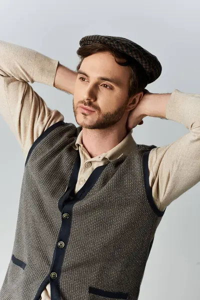 stock image A stylish man dressed in a classic vest and cap strikes a contemplative pose with elegance.