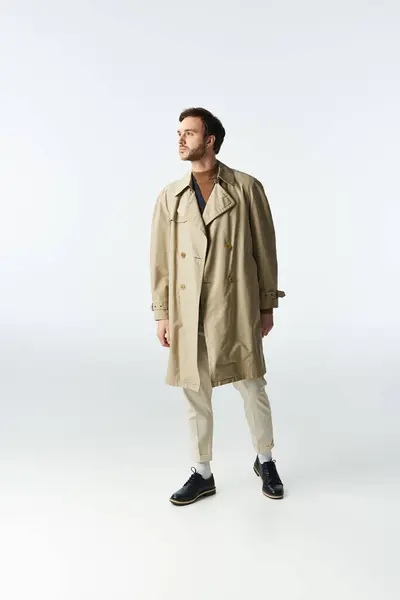 stock image A dapper man in a chic trench coat stands poised in an elegant setting.