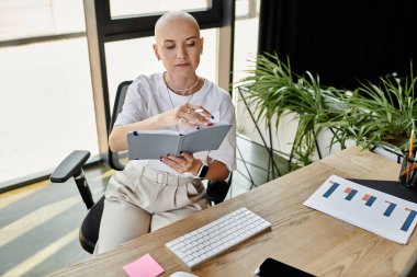 Şık bir ofis alanında, şık giyinmiş genç kel bir kadın notlarını dikkatle inceler..