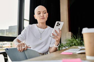 The young bald woman focuses on her phone while surrounded by a stylish office atmosphere. clipart