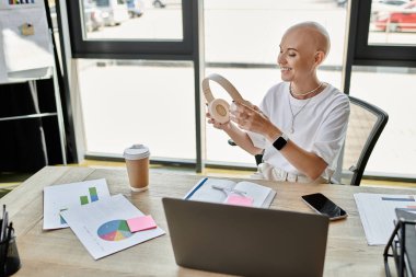 Kel kafalı dengeli bir kadın şık çalışma alanında kulaklık takıyor..