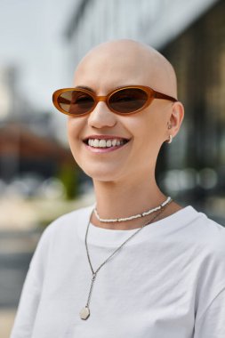 Şık güneş gözlüklü neşeli kel bir kadın aydınlık bir günün özünü yakalıyor..