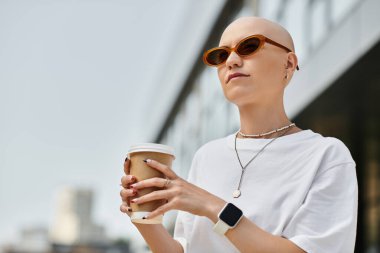 An elegant bald woman savors coffee outside, radiating confidence. clipart