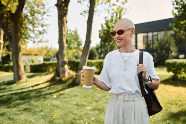 Zarif giyimli genç kadın, neşeli bir parkta yürüyor, içkisinin tadını çıkarıyor..