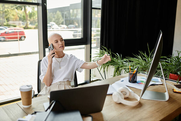 Молодая лысая женщина элегантно одетая разговаривает по телефону, окруженная зеленью и естественным светом.