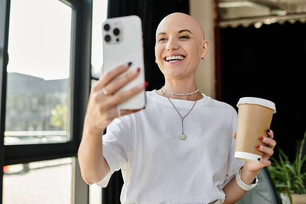 Молодая лысая женщина в элегантной одежде радостно пьет свой напиток и наслаждается моментом.